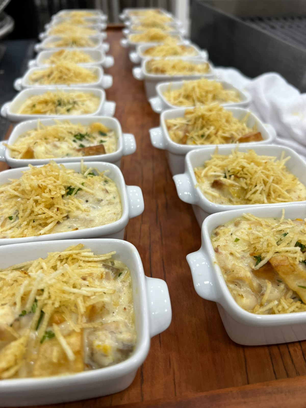 Fileiras de mini travessas de peixe gratinado com batata palha servidas como finger food em evento da HELÔ Events & Food